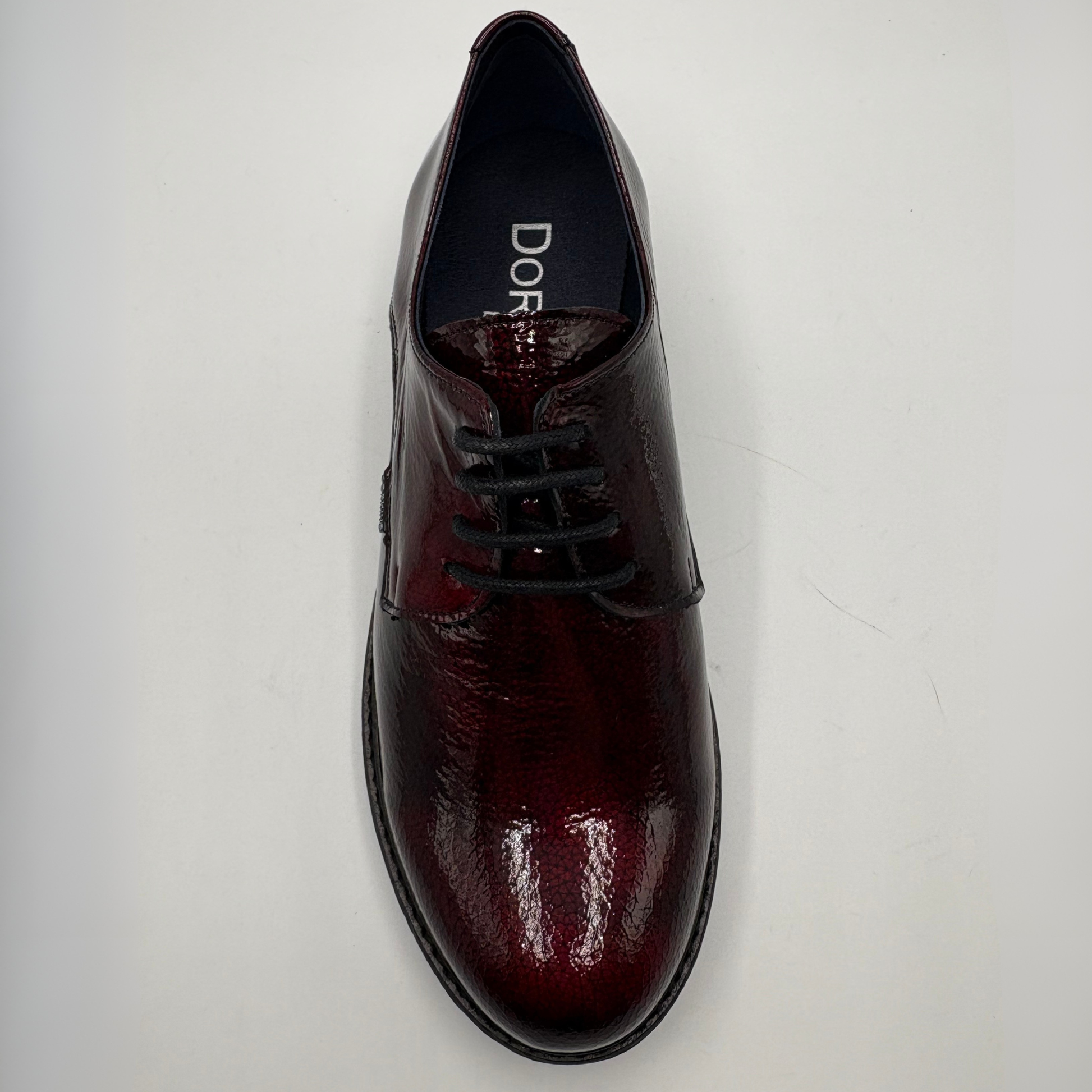 A single men's oxford-style dress shoe in glossy deep burgundy leather with black laces, photographed from above on a plain light background. The insole shows the brand name 'DORKING’