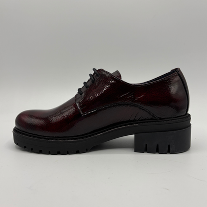A glossy dark burgundy patent leather lace-up oxford shoe with a chunky black platform sole, shown in a side profile against a neutral gray background.