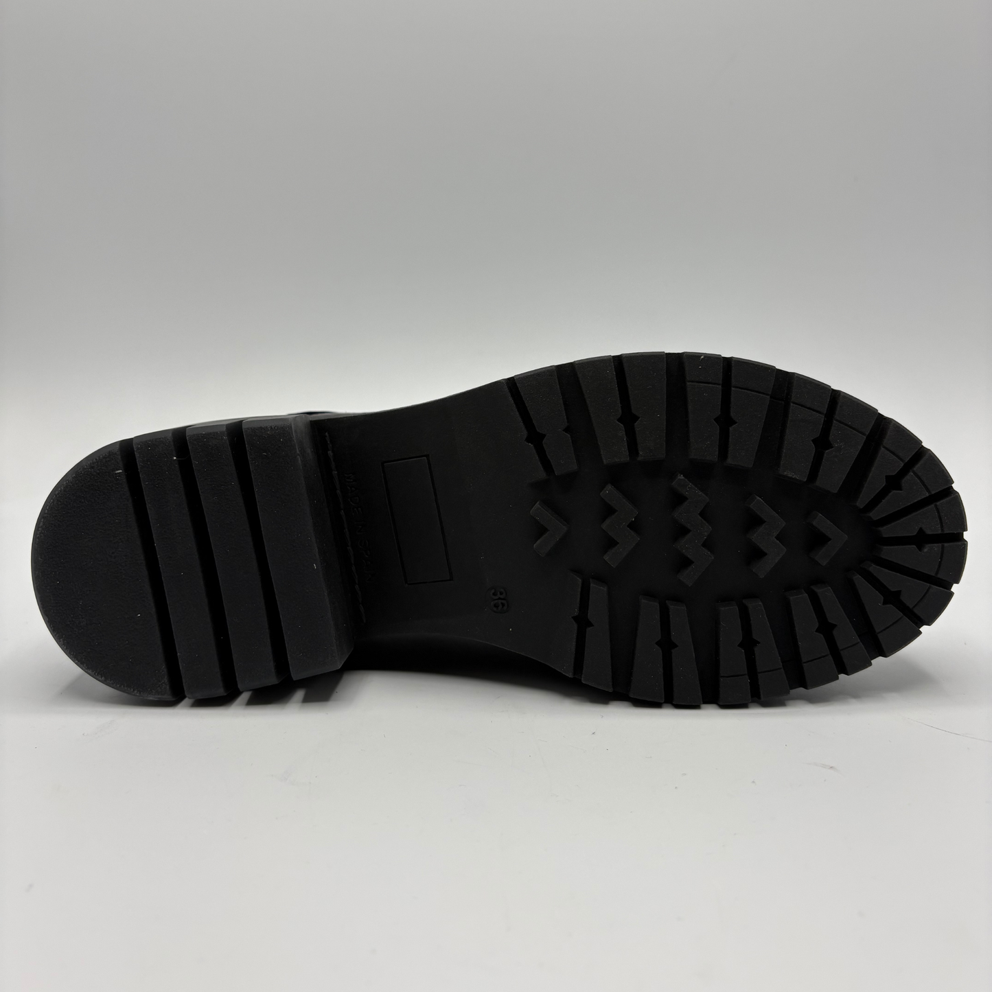 A close-up view of a black rubber boot sole, showing the tread pattern and heel structure, photographed against a neutral light gray background.
