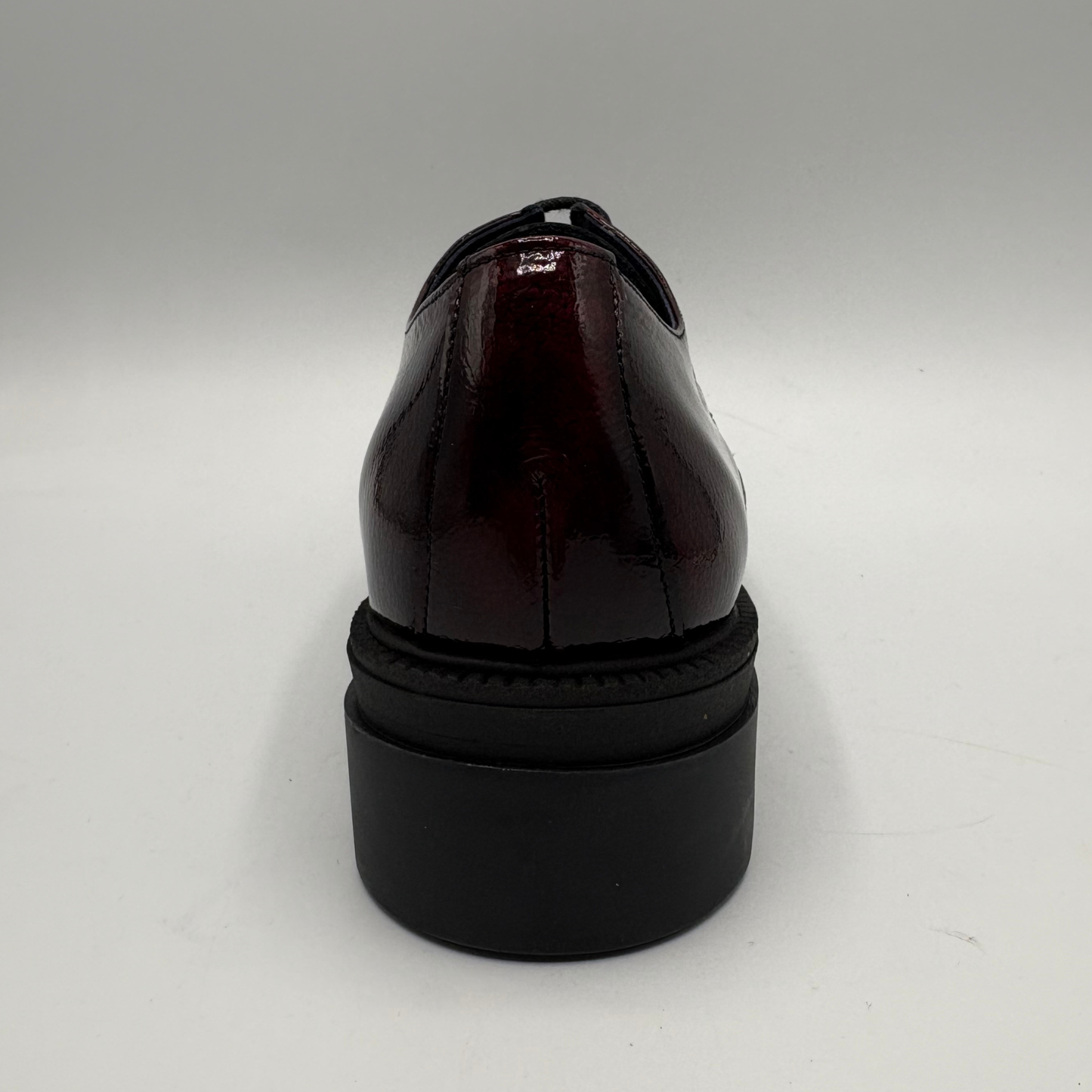A glossy dark burgundy patent leather oxford shoe shown from the back, featuring a chunky black platform sole.