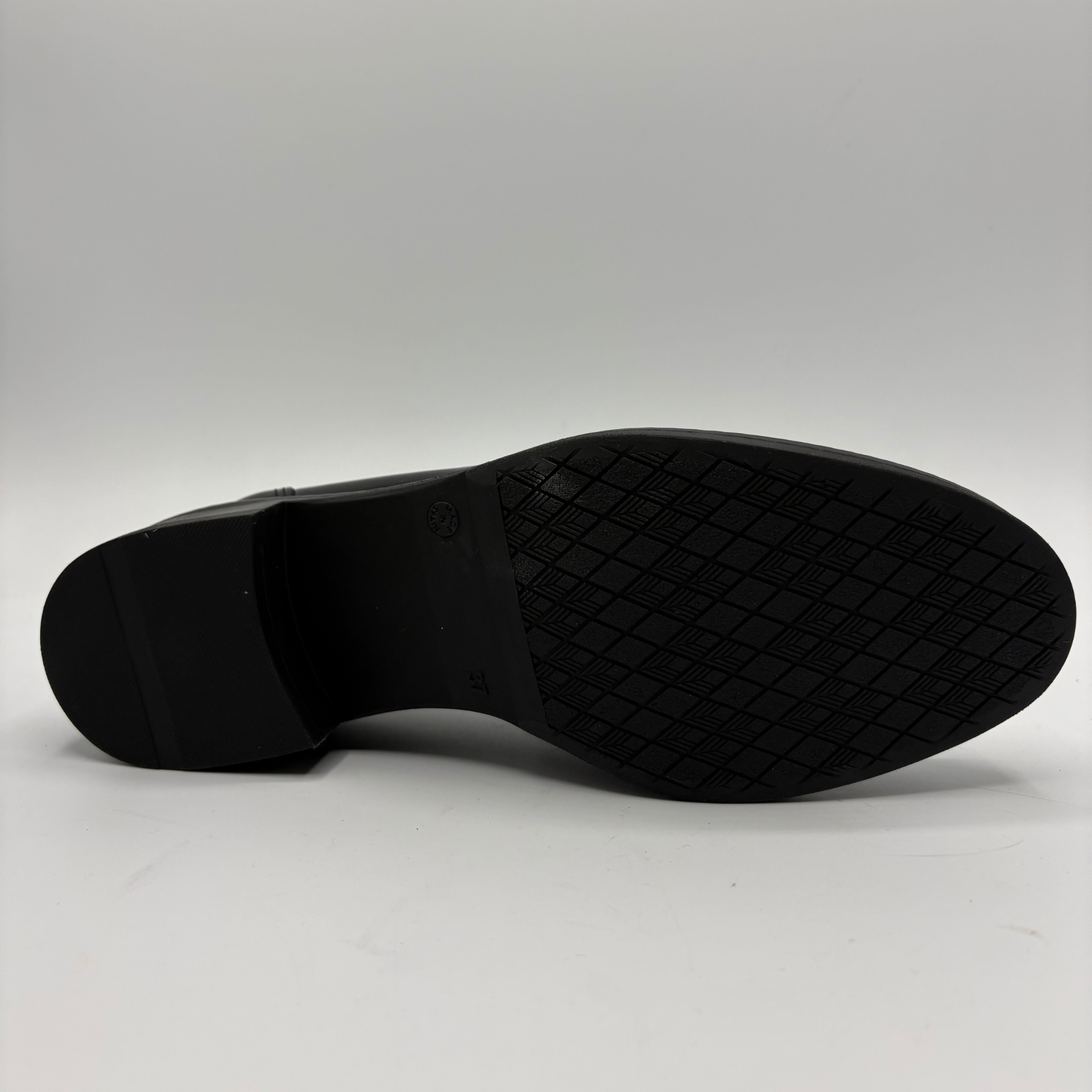 The black rubber outsole of a dress shoe, showing a textured diamond-pattern tread and a low block heel, photographed against a neutral light gray background.