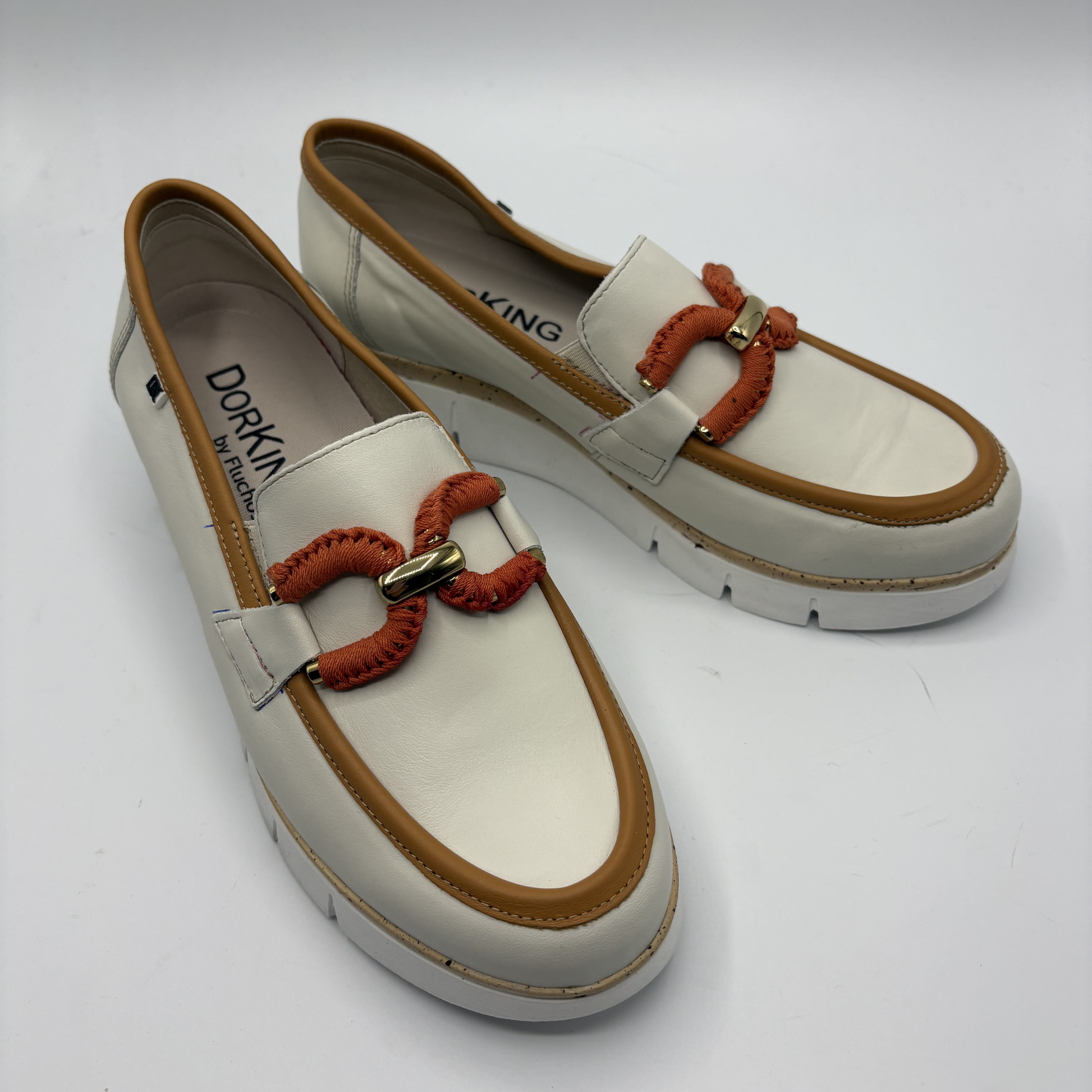 Pair of white loafers with brown accents and red braided details on a white background