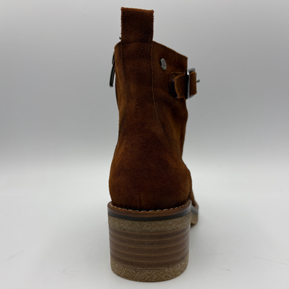 A brown suede ankle boot shown from the back, featuring a stacked brown and beige heel, a side buckle strap, and a zipper pull, photographed on a neutral gray background.