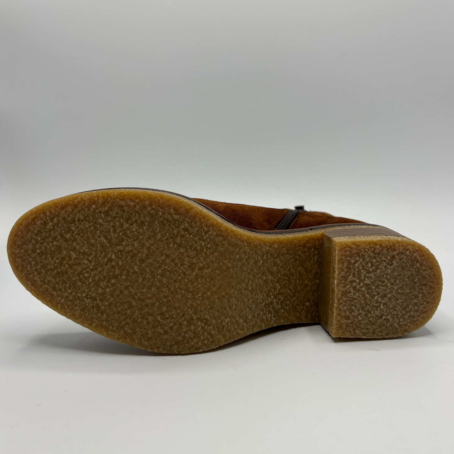 The textured brown rubber outsole and heel of a boot shown from a side profile view against a neutral gray studio background.