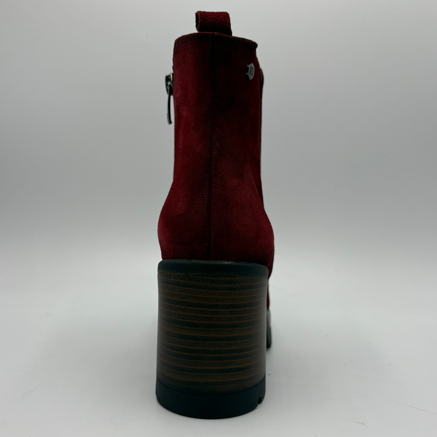 A single red suede ankle boot shown from the back, featuring a chunky dark brown and black striped block heel, a side zipper, and a small silver metal emblem on the back.