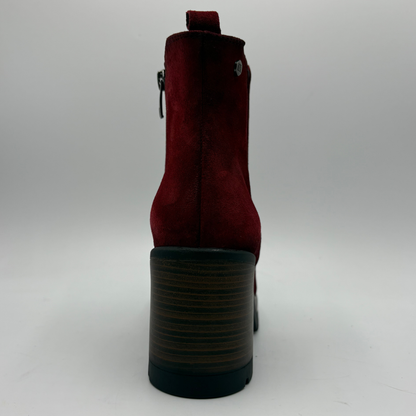 A single red suede ankle boot shown from the back, featuring a chunky dark brown and black striped block heel, a side zipper, and a small silver metal emblem on the back.