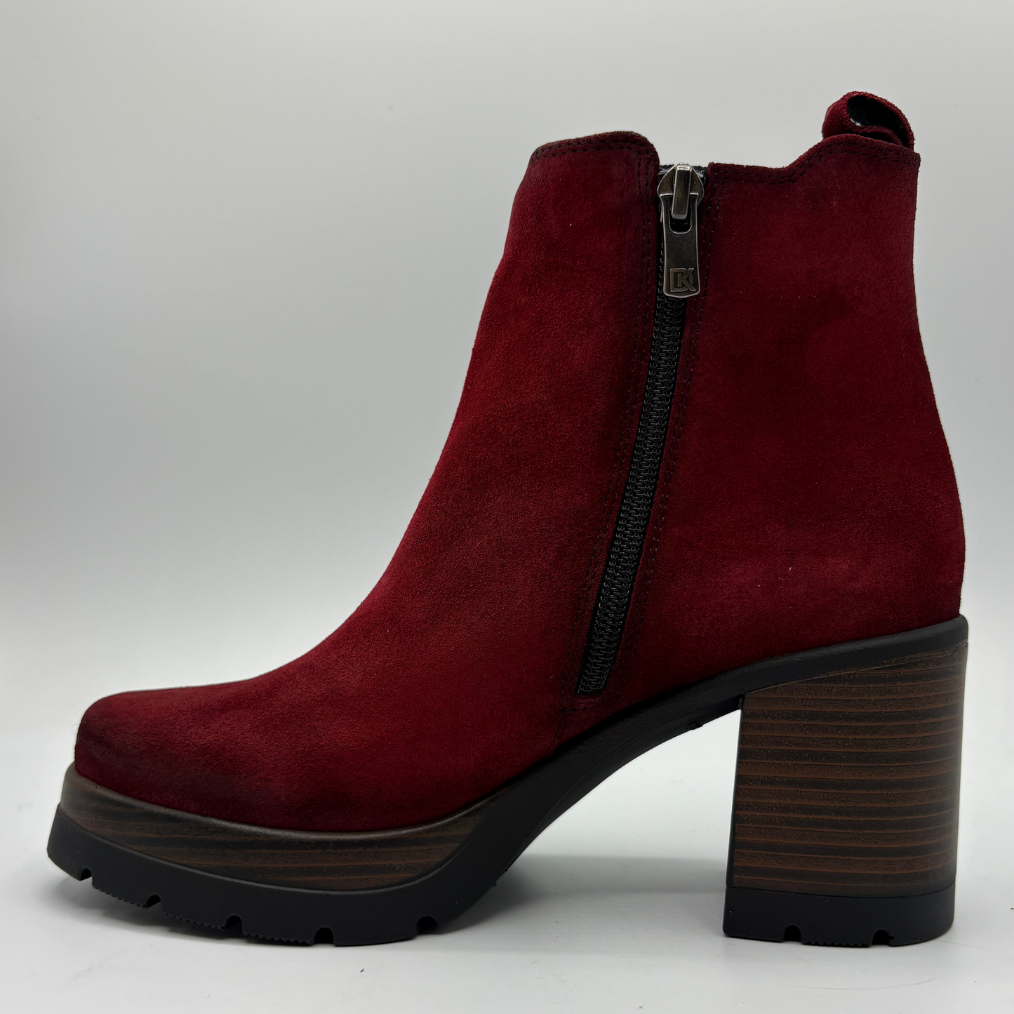 A single red suede ankle boot with a high block heel, black side zipper, and a dark wood-look sole, shown against a light gray background.
