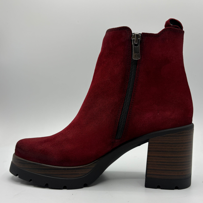 A single red suede ankle boot with a high block heel, black side zipper, and a dark wood-look sole, shown against a light gray background.