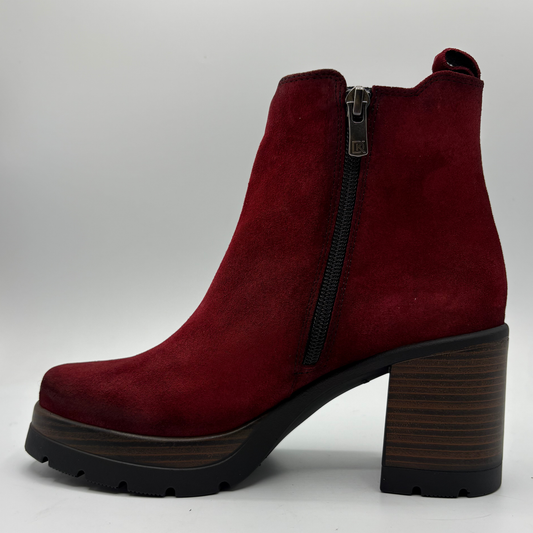 A single red suede ankle boot with a high block heel, black side zipper, and a dark wood-look sole, shown against a light gray background.