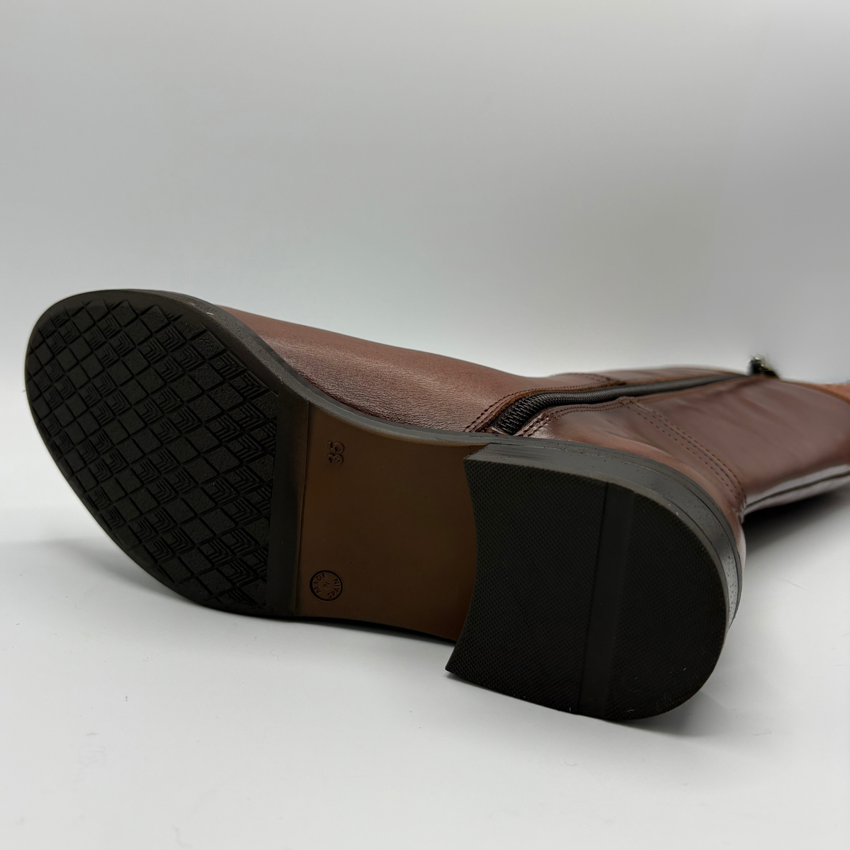 Bottom view of a tall brown leather boot with a decorative buckle and low black heel