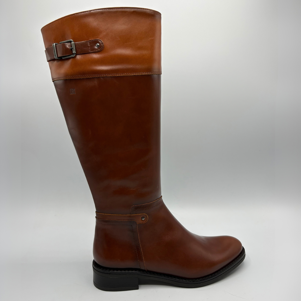 Right facing view of a tall brown leather boot with a decorative buckle and low black heel