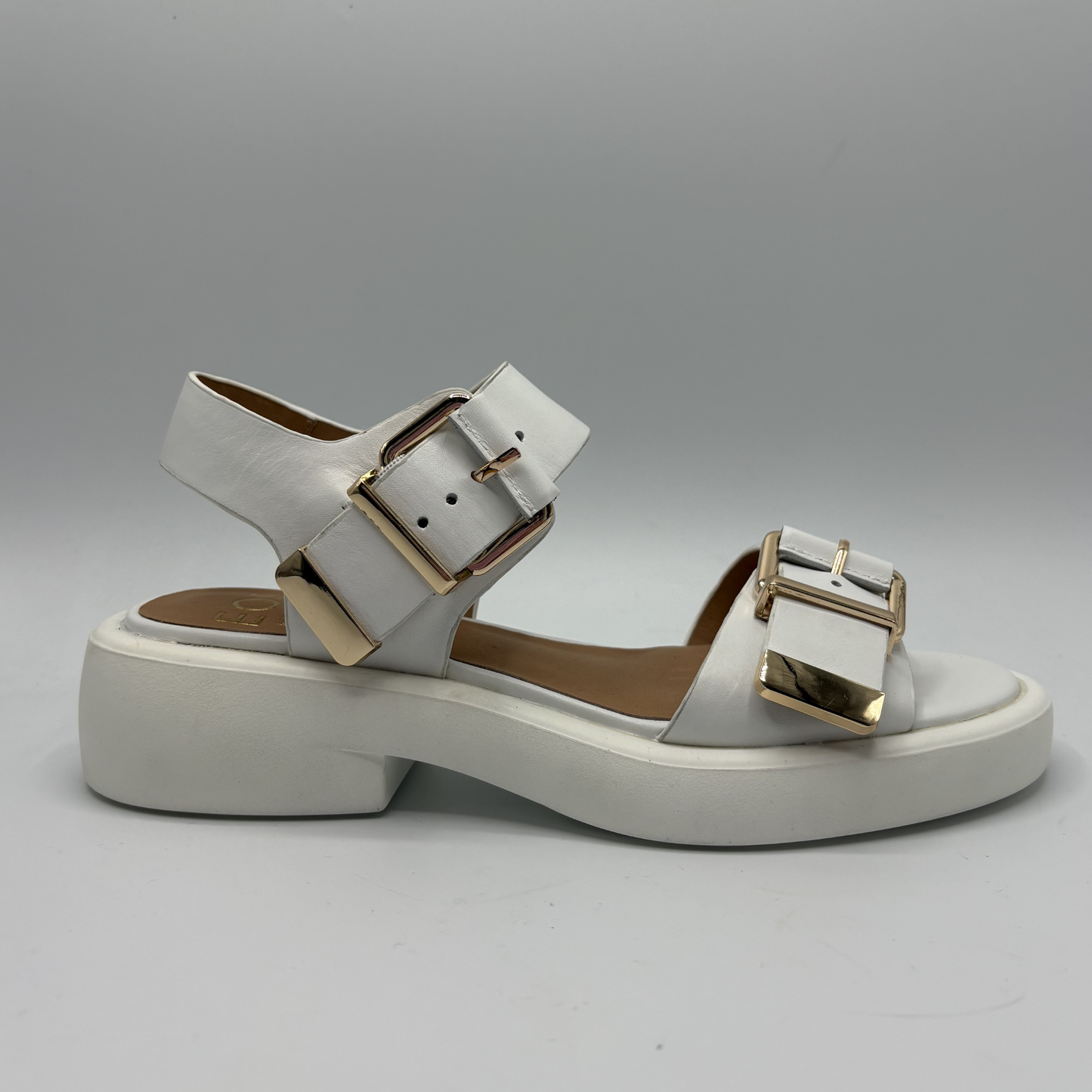 White sandal with gold buckles on a gray background