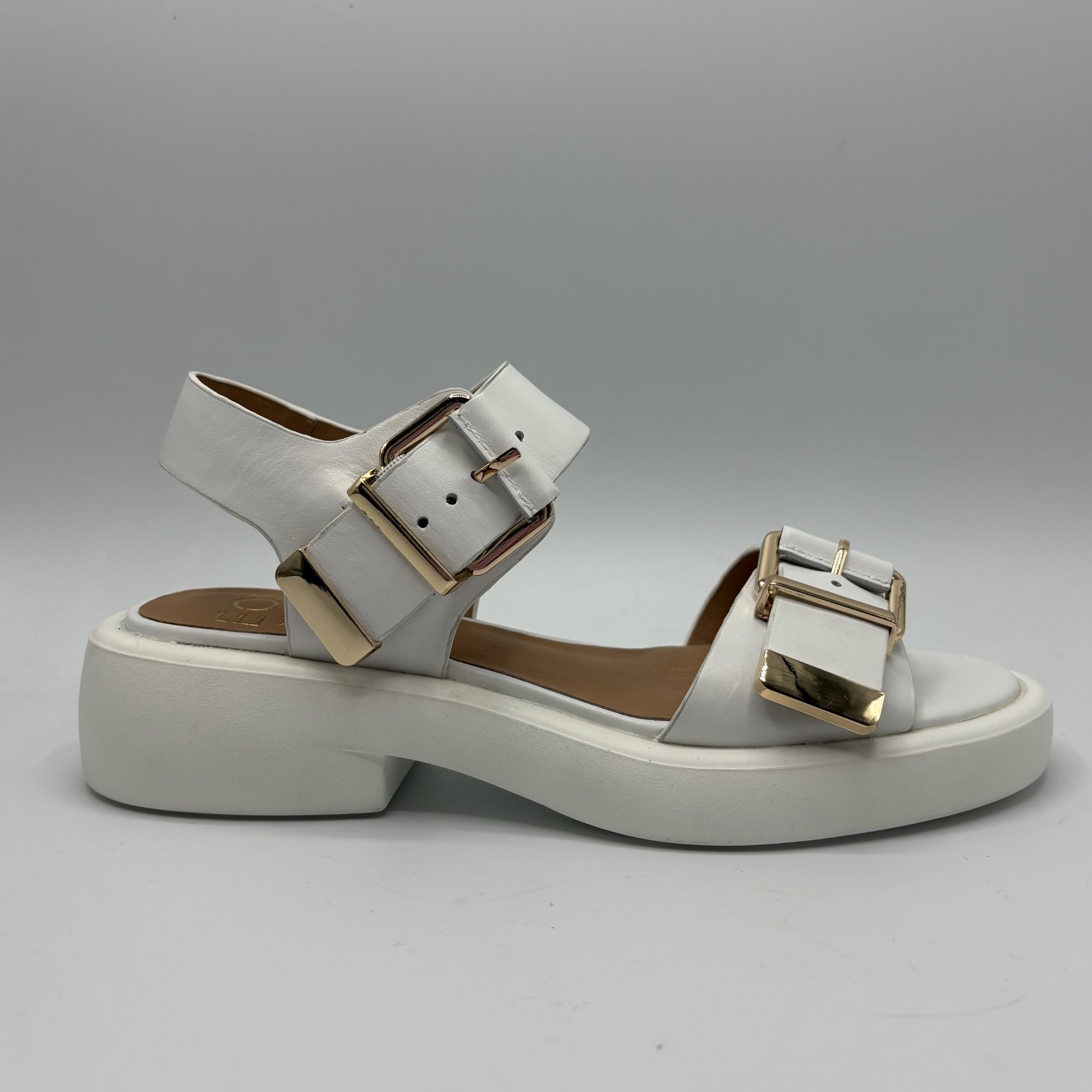 White sandal with gold buckles on a gray background