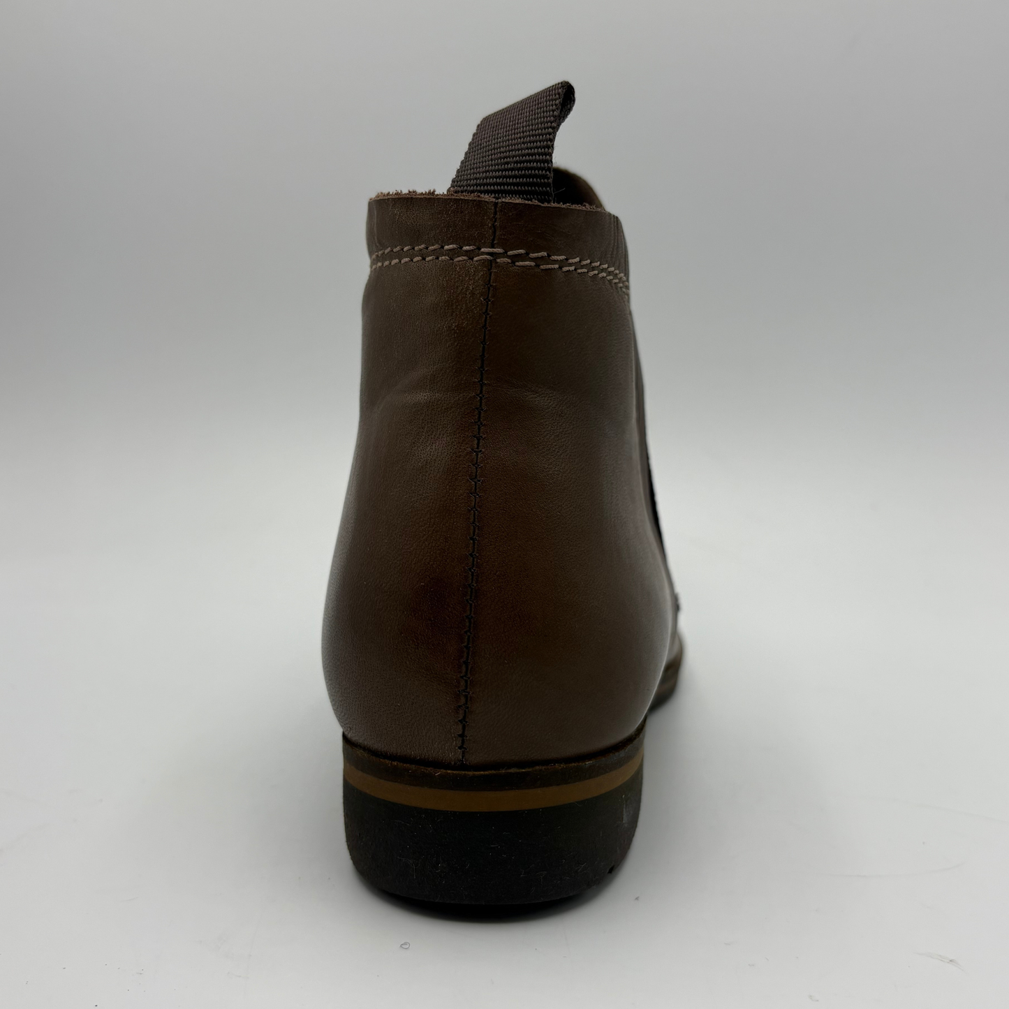 A dark brown leather ankle boot shown from the back, featuring a pull tab, contrast stitching, and a black sole with a tan stripe.
