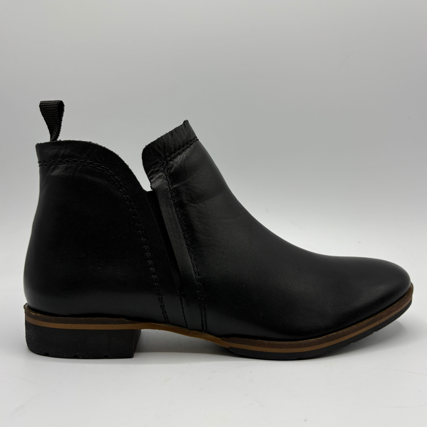 A black leather Chelsea ankle boot with a low block heel and a pull tab, shown from a side profile view on a light gray background.