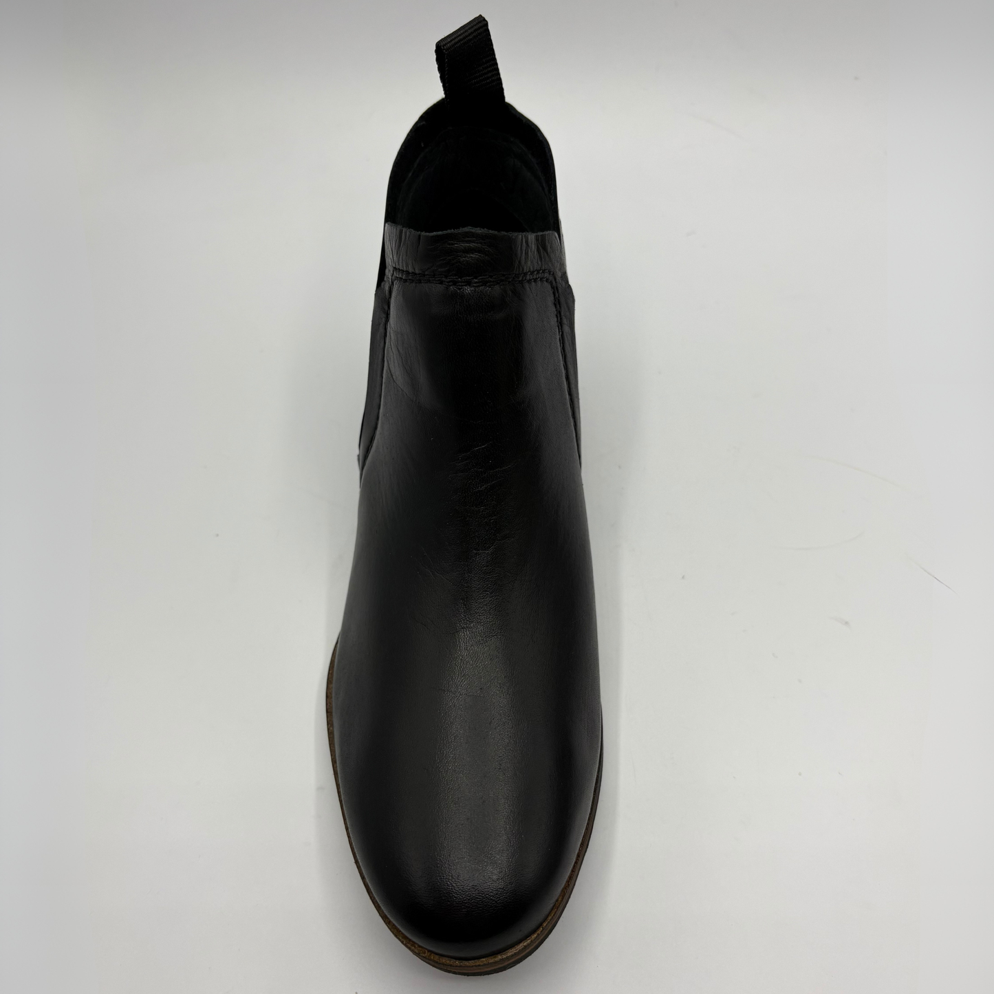 A single black leather Chelsea boot with a pull tab, shown from a top-down perspective on a light gray background.