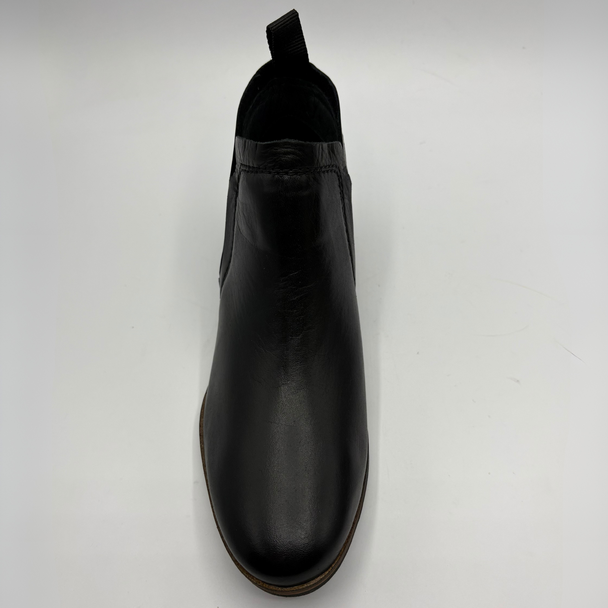 A single black leather Chelsea boot with a pull tab, shown from a top-down perspective on a light gray background.