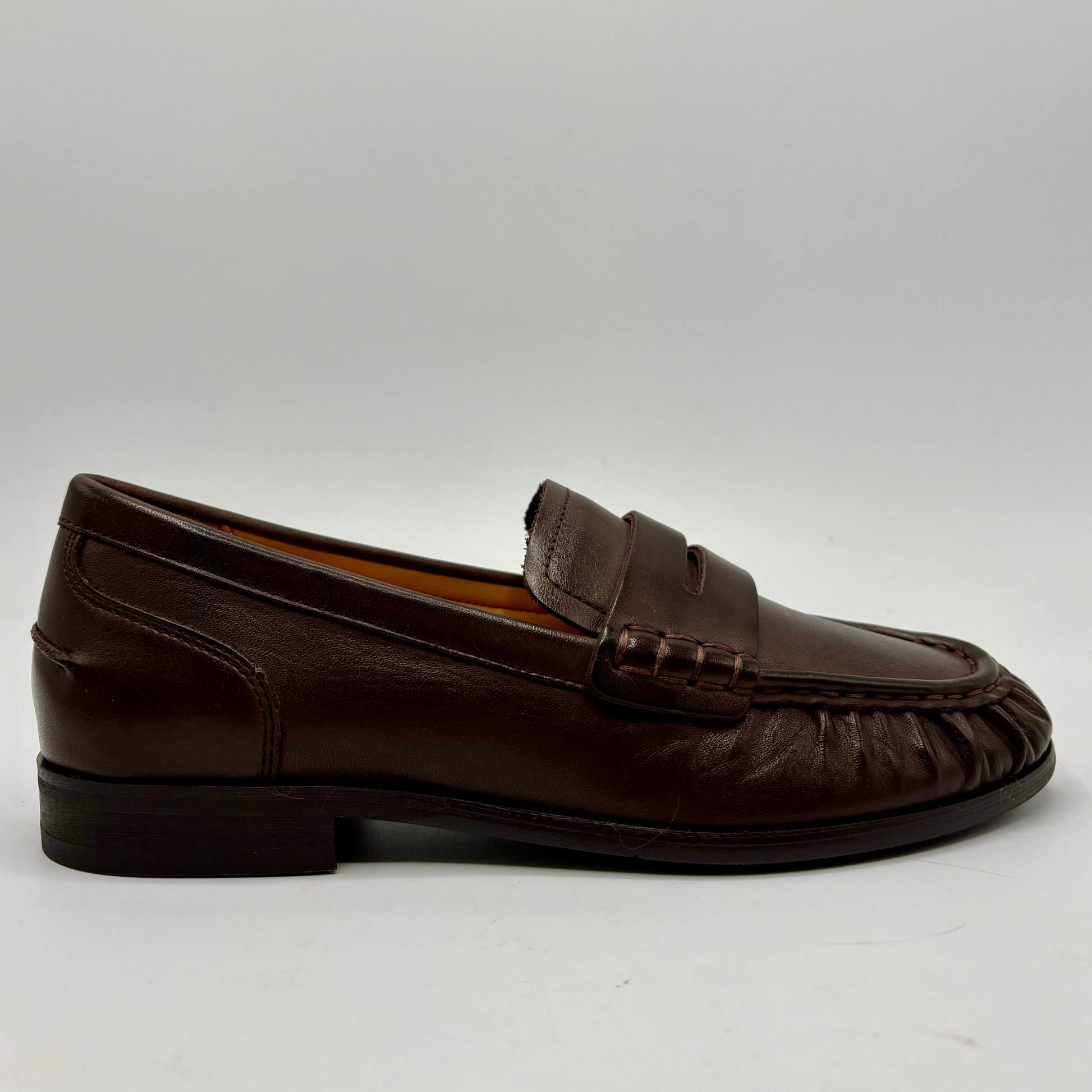 A single dark brown leather penny loafer shown in profile against a light gray background.