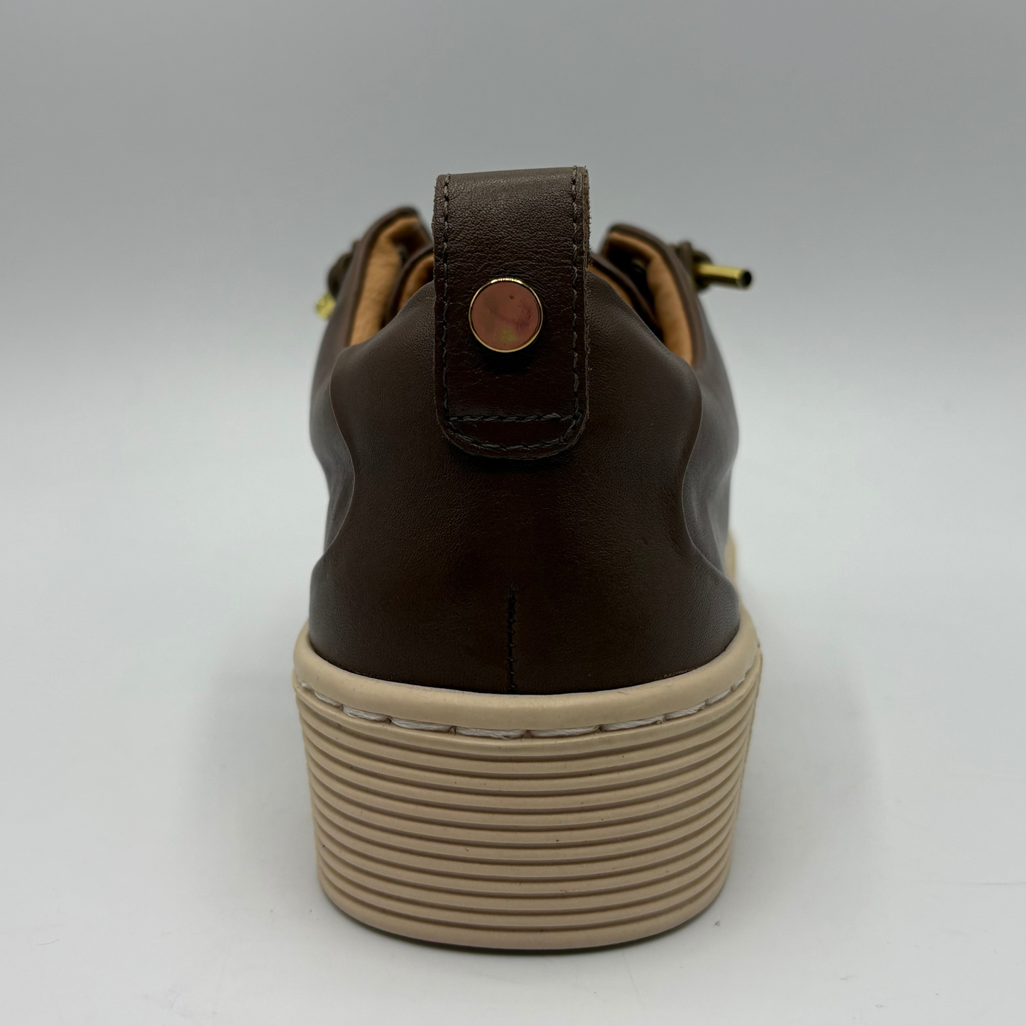 A close-up rear view of a brown leather shoe with a chunky beige platform sole and a small metallic pull tab on the heel.