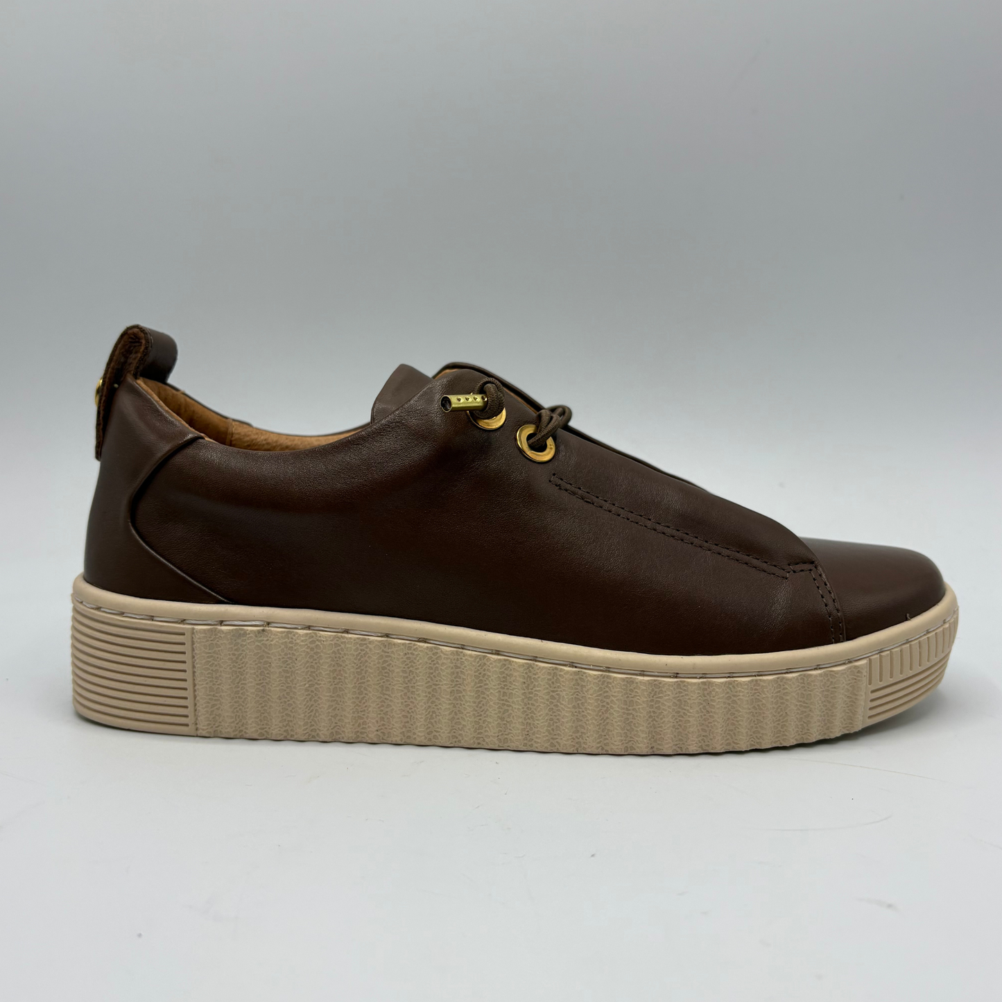 A dark brown leather low-top sneaker with a chunky beige platform sole and gold-tone eyelets, shown from a side profile on a light gray background.