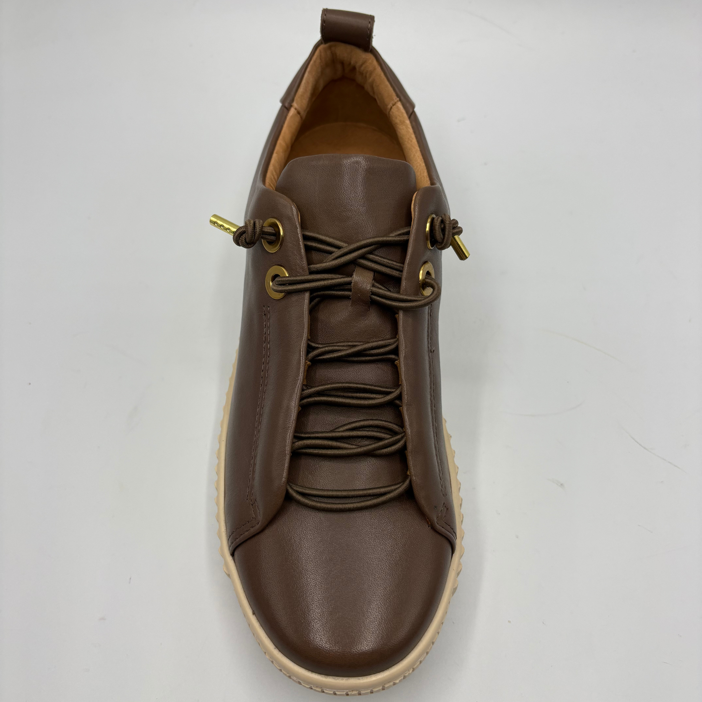 A brown leather lace-up sneaker with gold-tone metal eyelets and a beige rubber sole, photographed from a top-down angle on a light gray background.