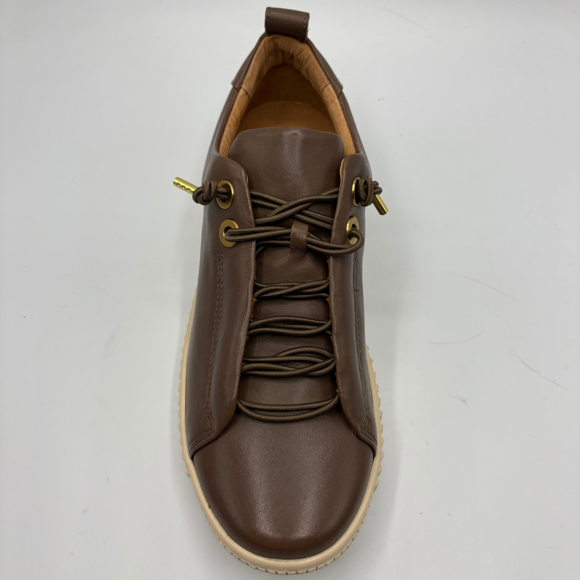 A brown leather lace-up sneaker with gold-tone metal eyelets and a beige rubber sole, photographed from a top-down angle on a light gray background.