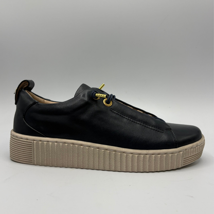 A black leather platform sneaker with a beige ribbed sole and gold-tone eyelets, shown from a side profile on a neutral gray background.