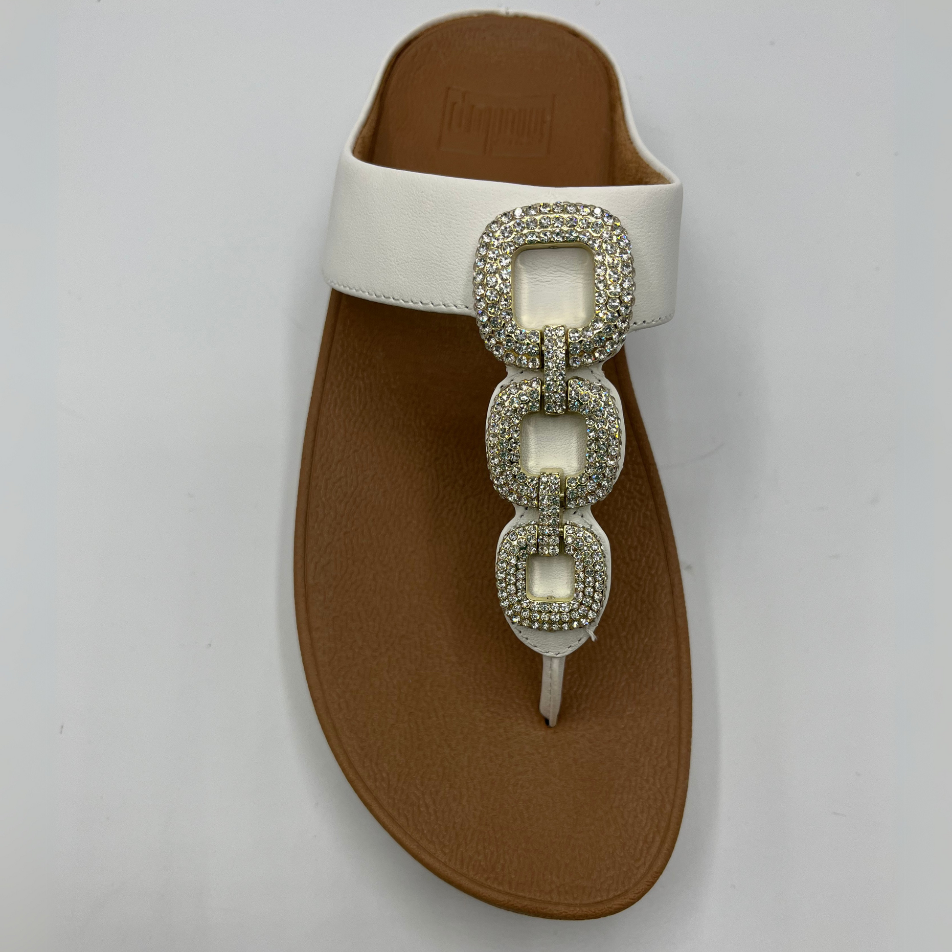Top view of a leather wedge sandal with a white strap and toe post. Featuring a crystal chain detail on the strap.