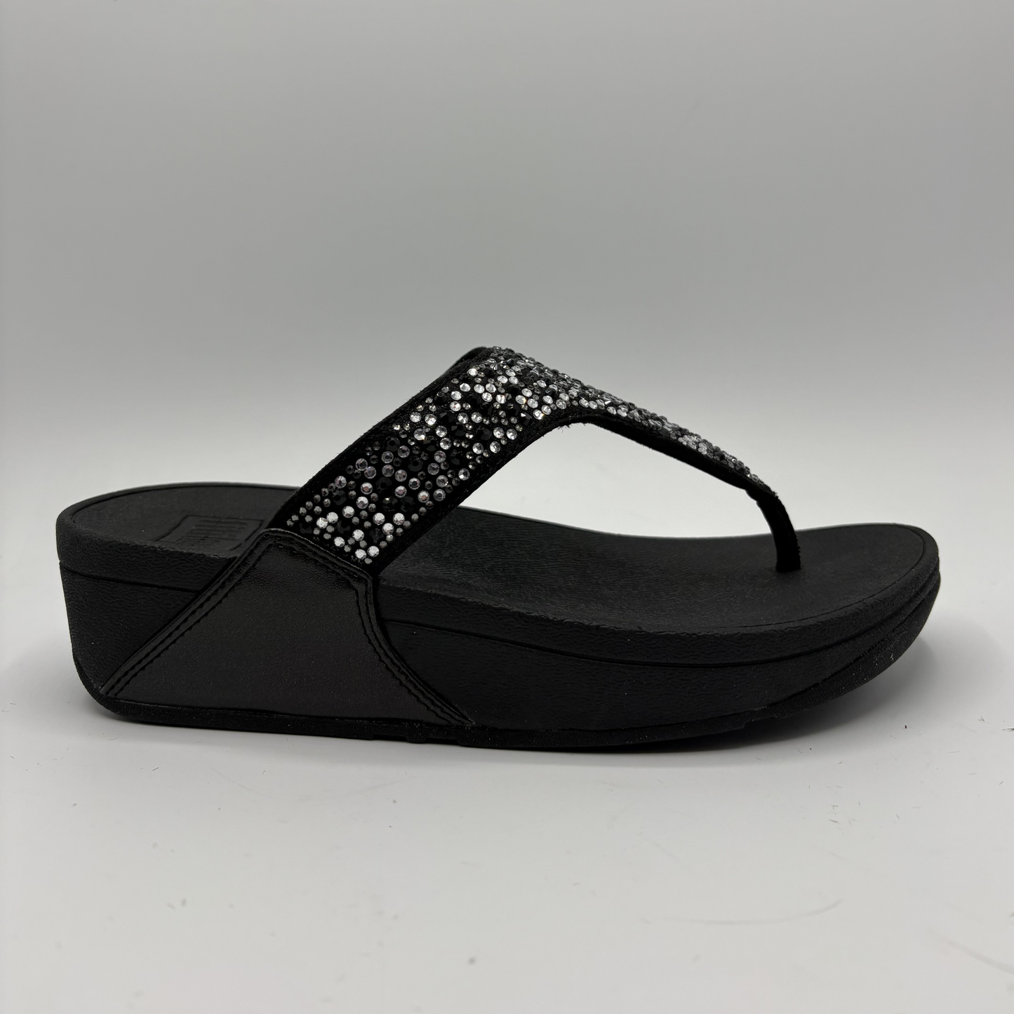 Black sandal with rhinestone embellishments on a gray background