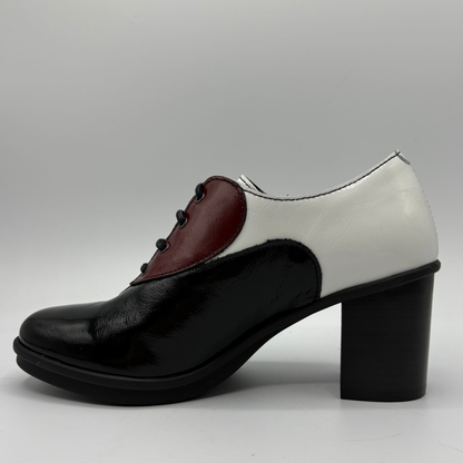A women's block-heel oxford shoe with a colorblock design, featuring a glossy black toe and heel, a white side panel, and a burgundy leather vamp section with black laces, shown against a neutral gray background.