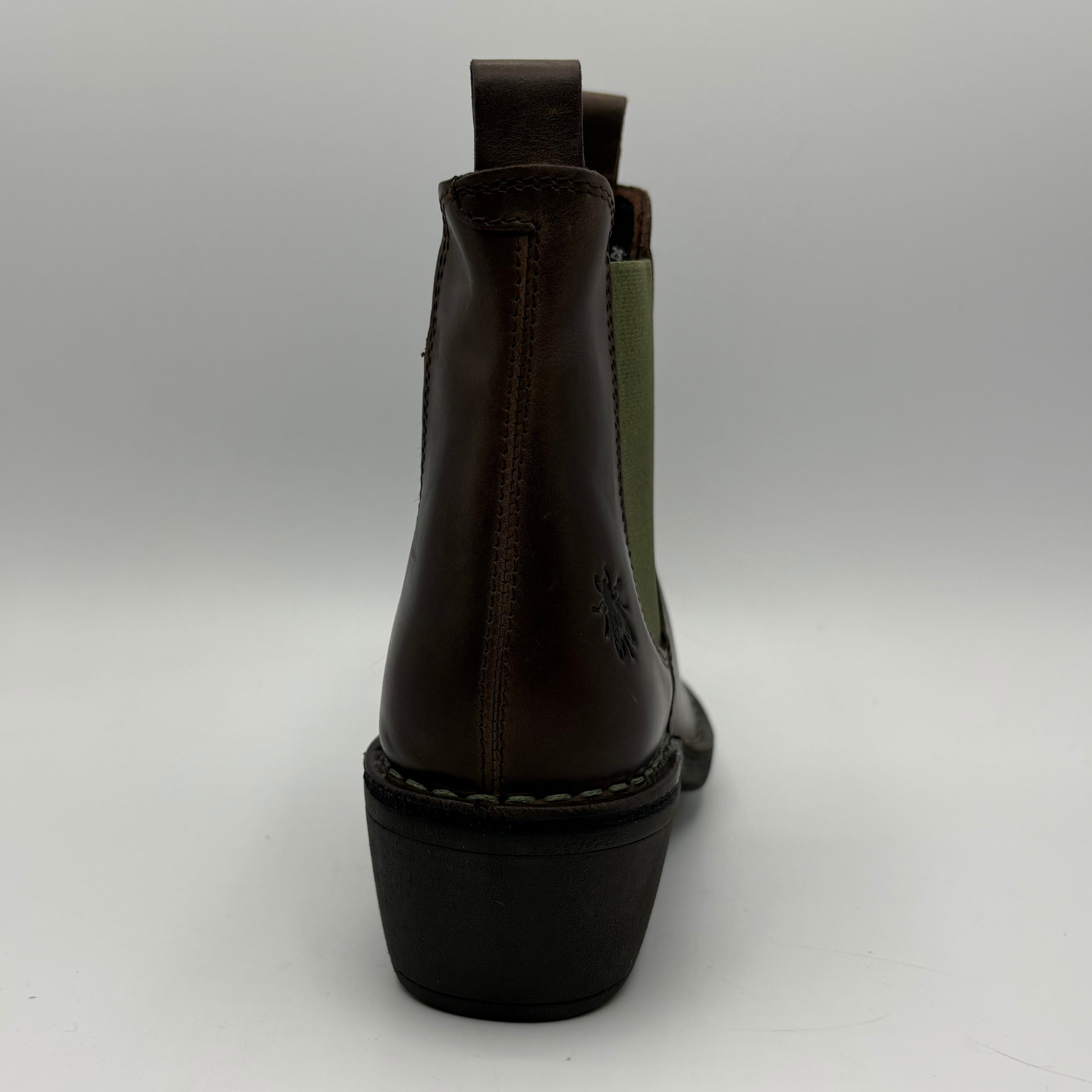 A dark brown leather ankle boot shown from the back, featuring a black block heel, contrast stitching, and a muted olive green elastic side panel on a light gray background.