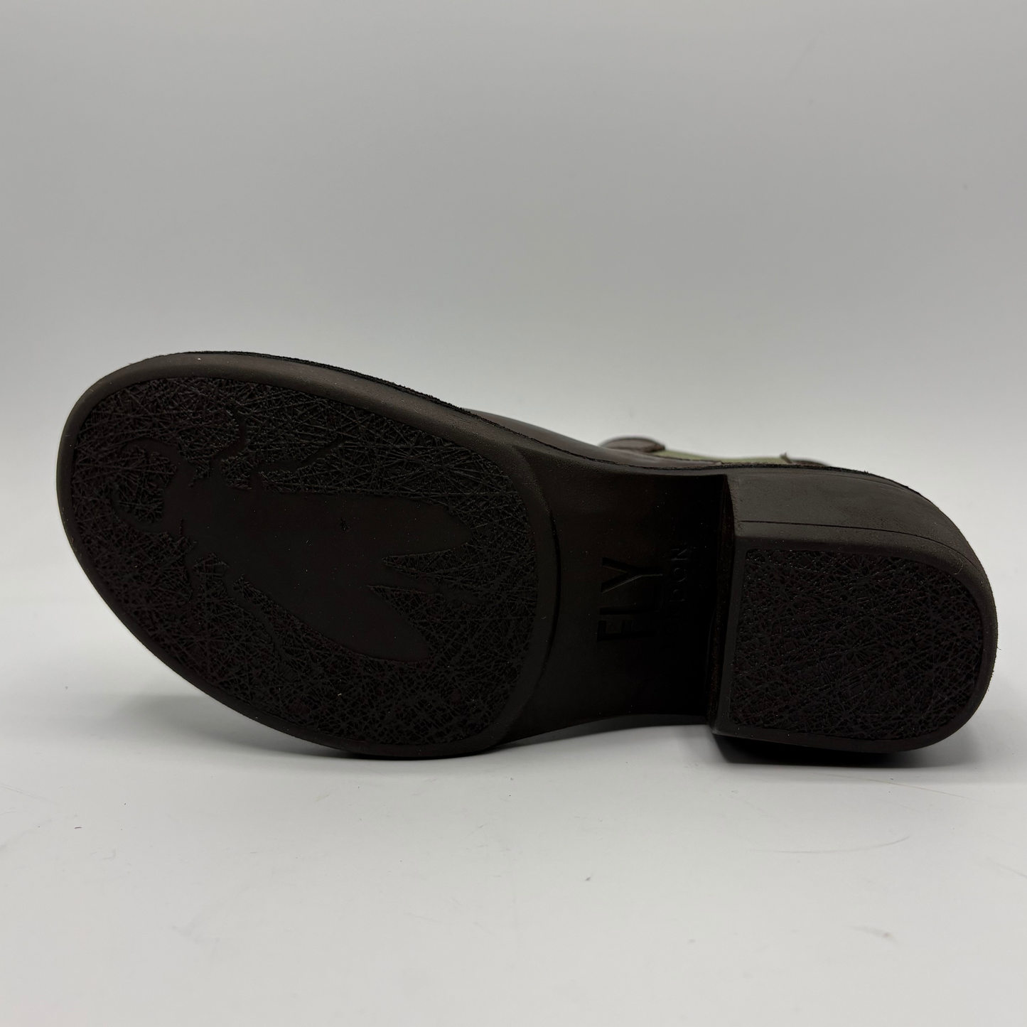 The black rubber outsole of a boot, showing a textured tread pattern and embossed branding, photographed against a neutral light gray background.