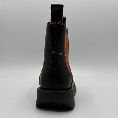 A black leather ankle boot shown from the back, featuring contrast stitching, a tan elastic side panel, and a chunky black sole on a light gray background.