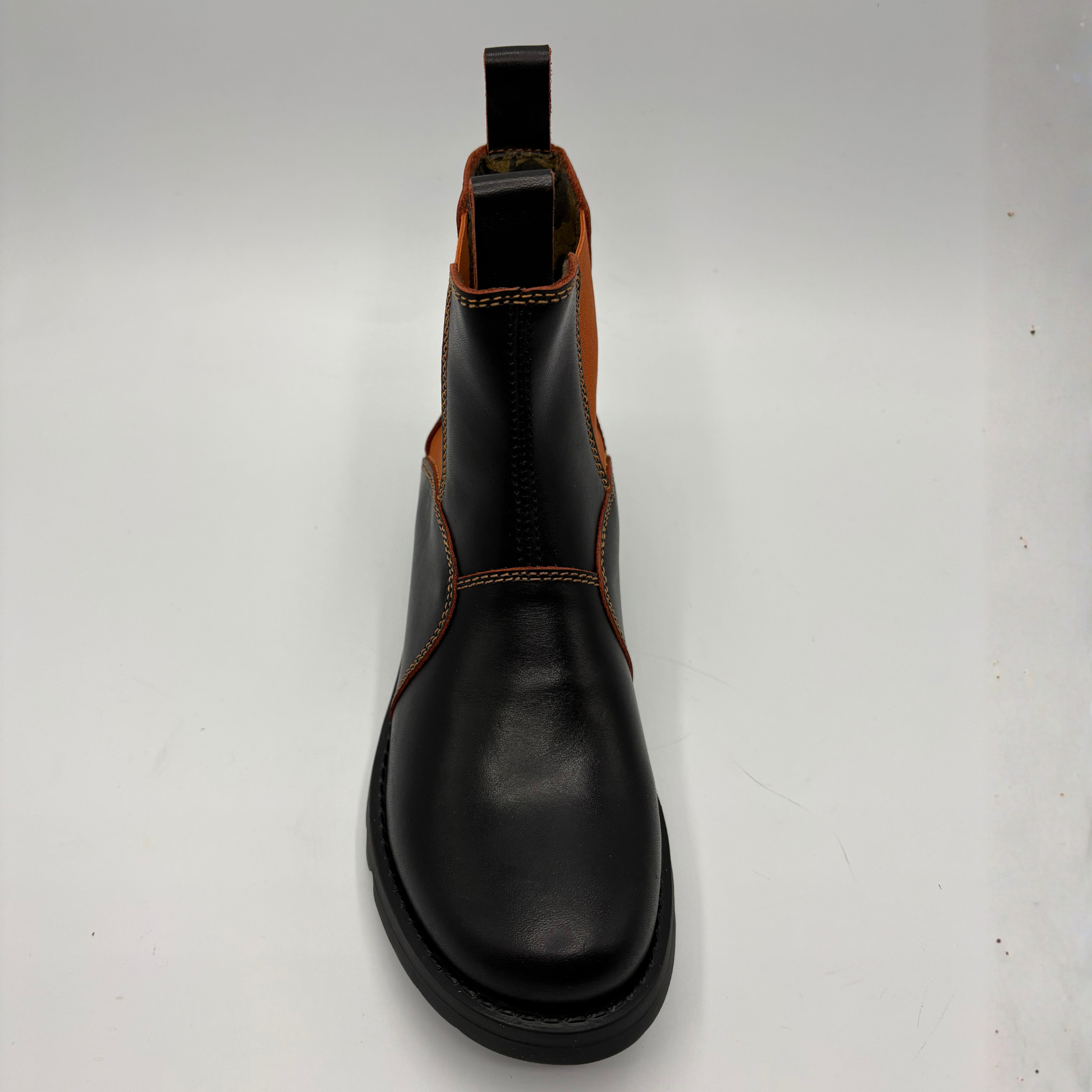 A black leather Chelsea boot with contrast orange stitching and a brown elastic side panel, shown from a top-down view on a white background.