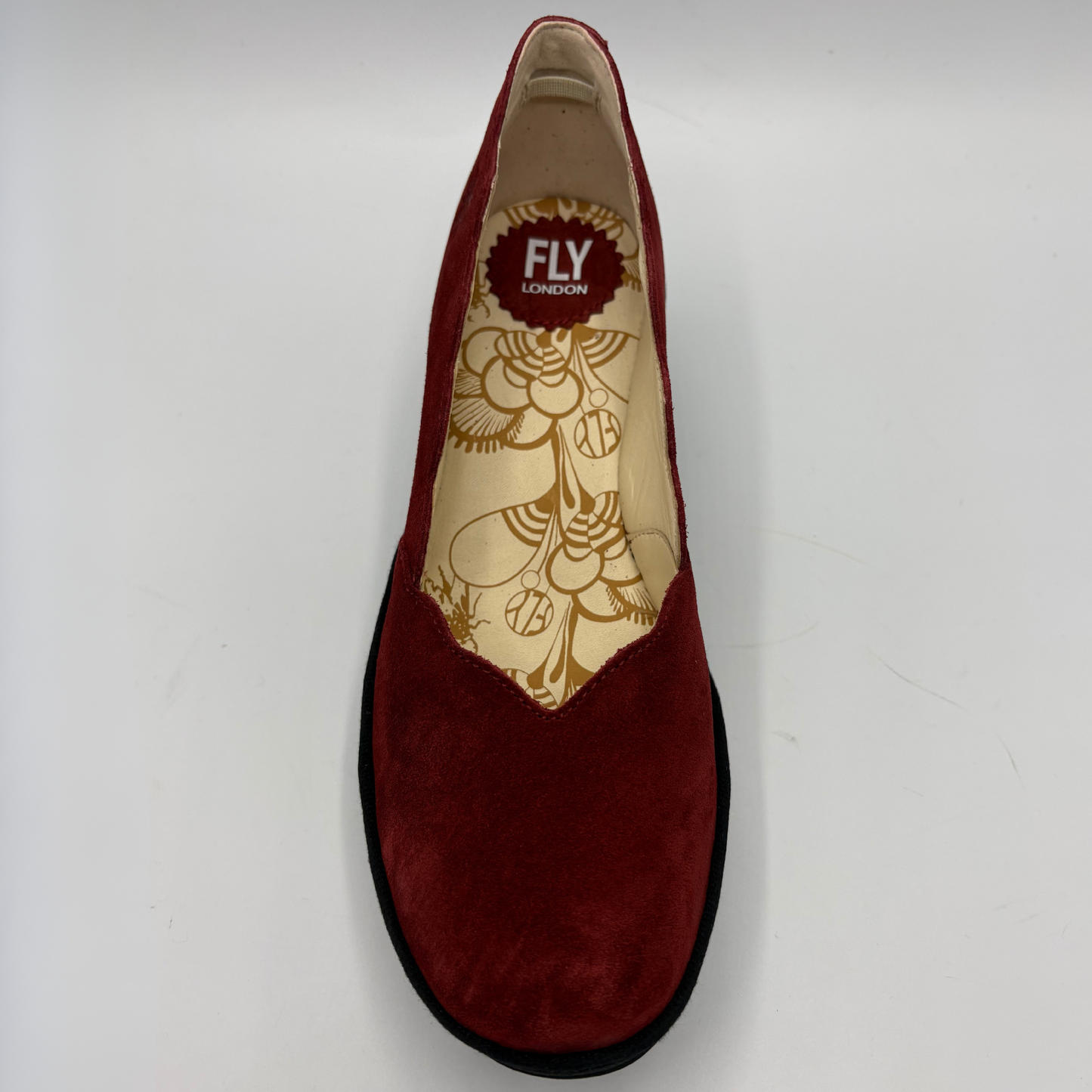 A single red suede slip-on shoe shown from a top-down view on a light gray background. The insole is cream-colored with a gold floral pattern and features a red circular logo that reads 'FLY LONDON'.