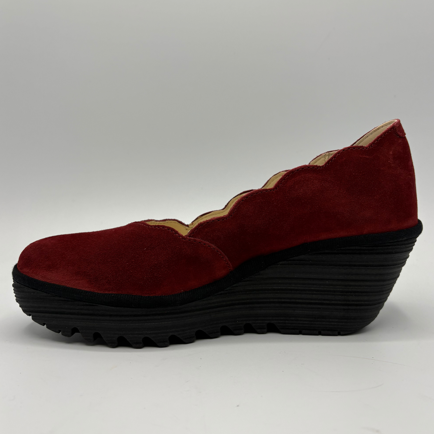 A single women's wedge shoe in deep burgundy suede with a scalloped edge detail and a thick black ridged wedge sole, shown from a side profile on a light gray background.