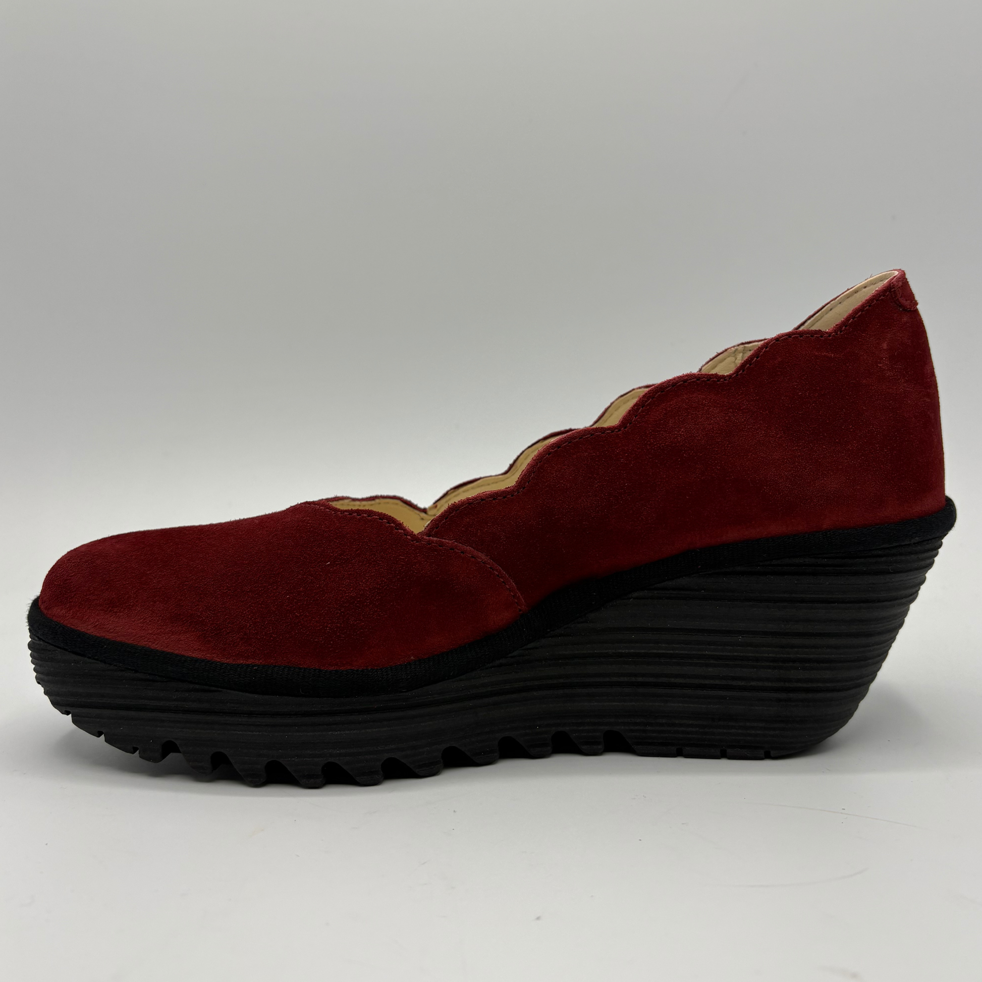 A single women's wedge shoe in deep burgundy suede with a scalloped edge detail and a thick black ridged wedge sole, shown from a side profile on a light gray background.