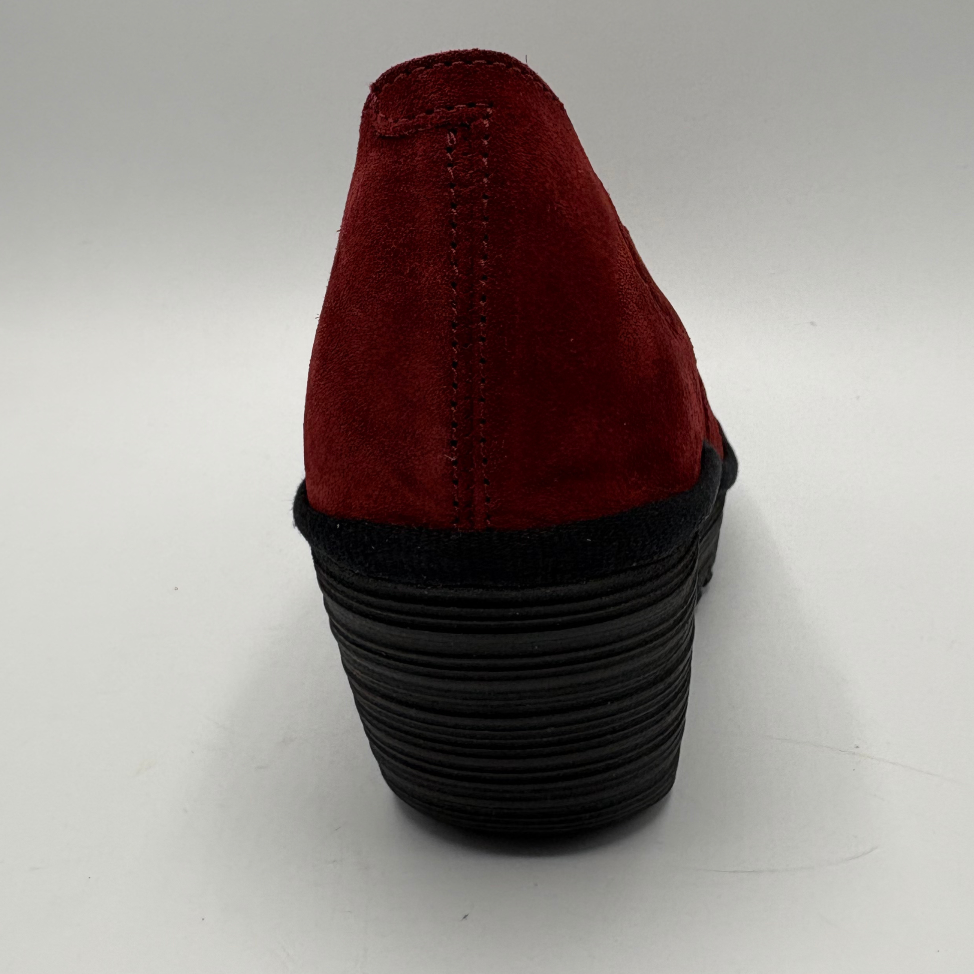 A single red suede shoe shown from the back, featuring a deep red suede upper and a thick, black ridged platform heel, set against a plain light gray background.