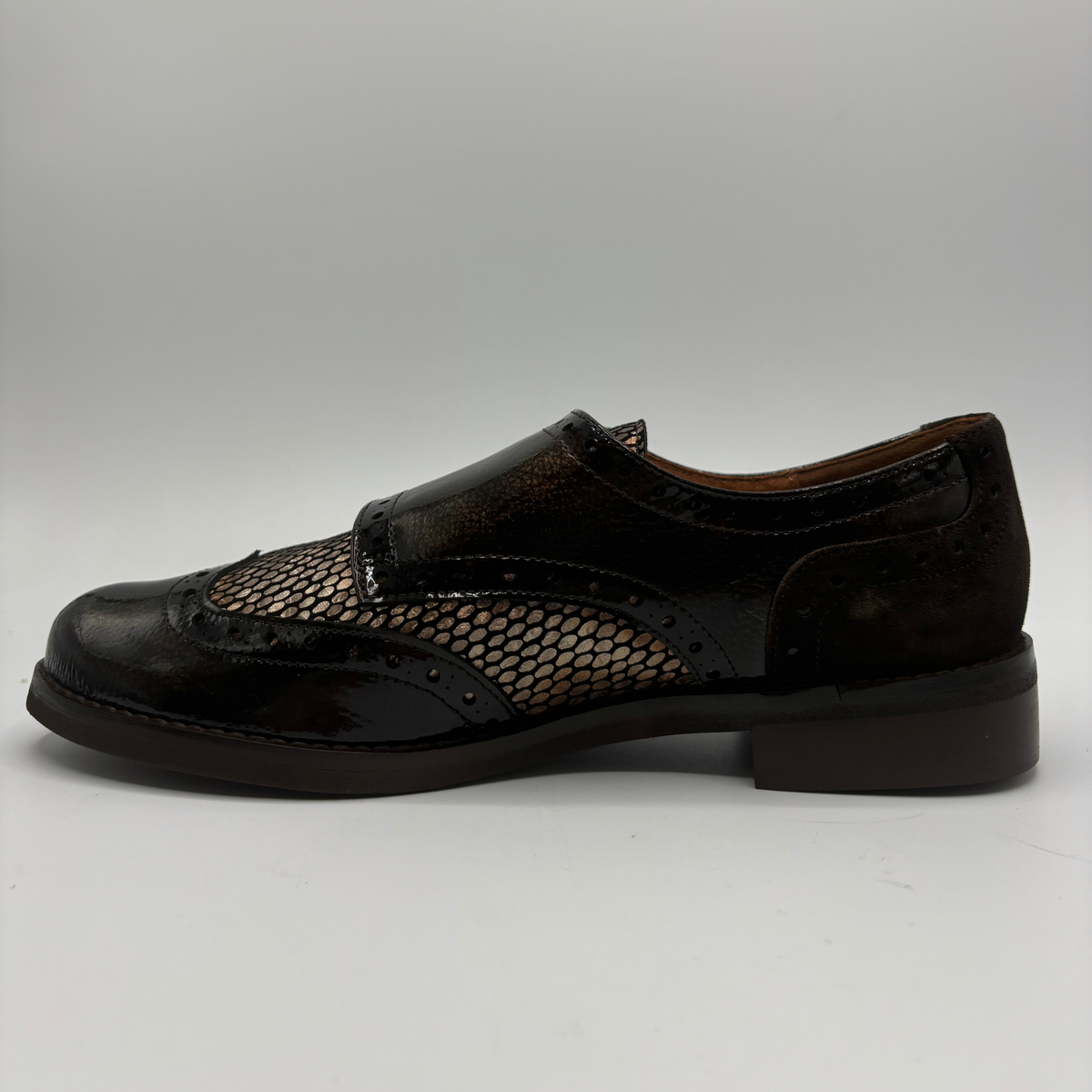 Left facing view of a shoe with a low heel, leather upper and decorative gold buckles on a white background