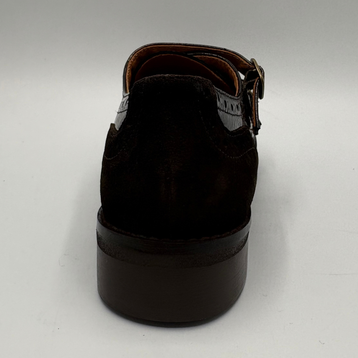 Back view of a shoe with a low heel, leather upper and decorative gold buckles on a white background