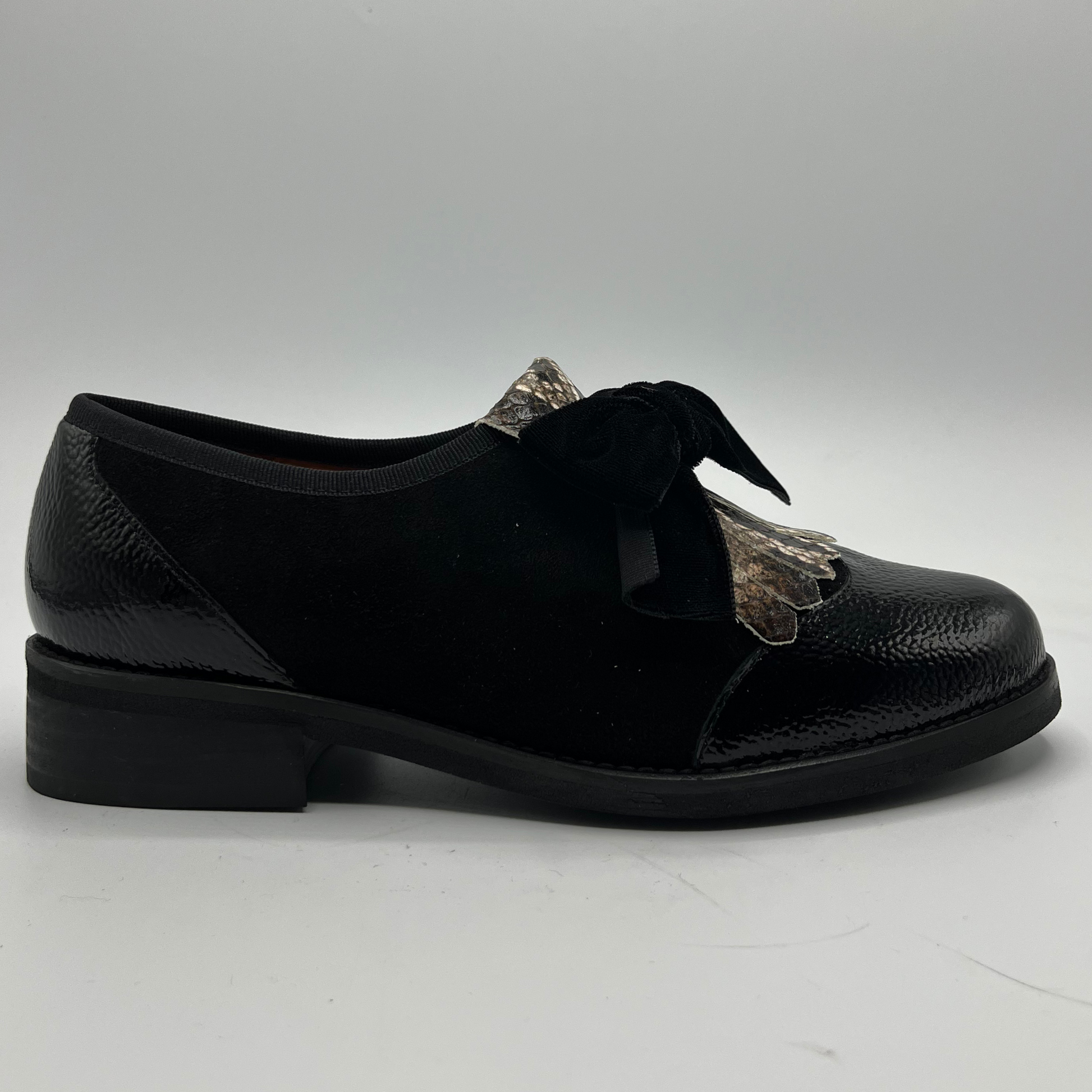 Black leather shoe with decorative bow on a white background