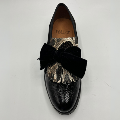 Black loafer shoe with snake print and black bow on a light gray background