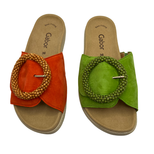 Top view of a pair of suede slides, One is orange and one is lime green. Both have a large buckle detail and anatomical footbed