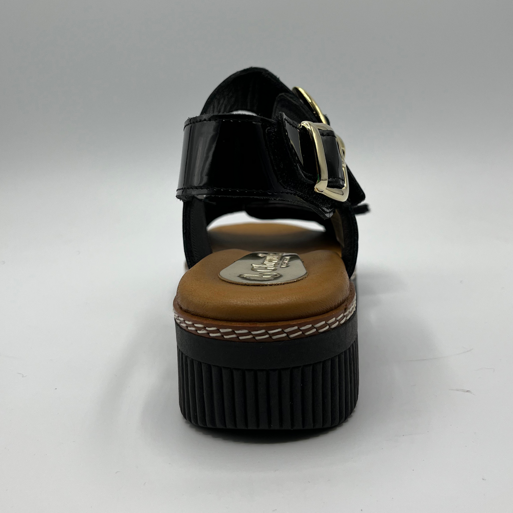 Back view of a black patent leather sandal with decorative gold buckles and a wedge heel.