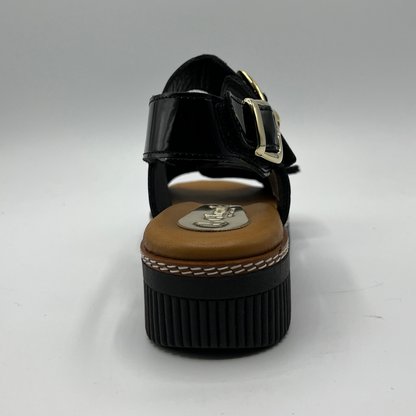 Back view of a black patent leather sandal with decorative gold buckles and a wedge heel.