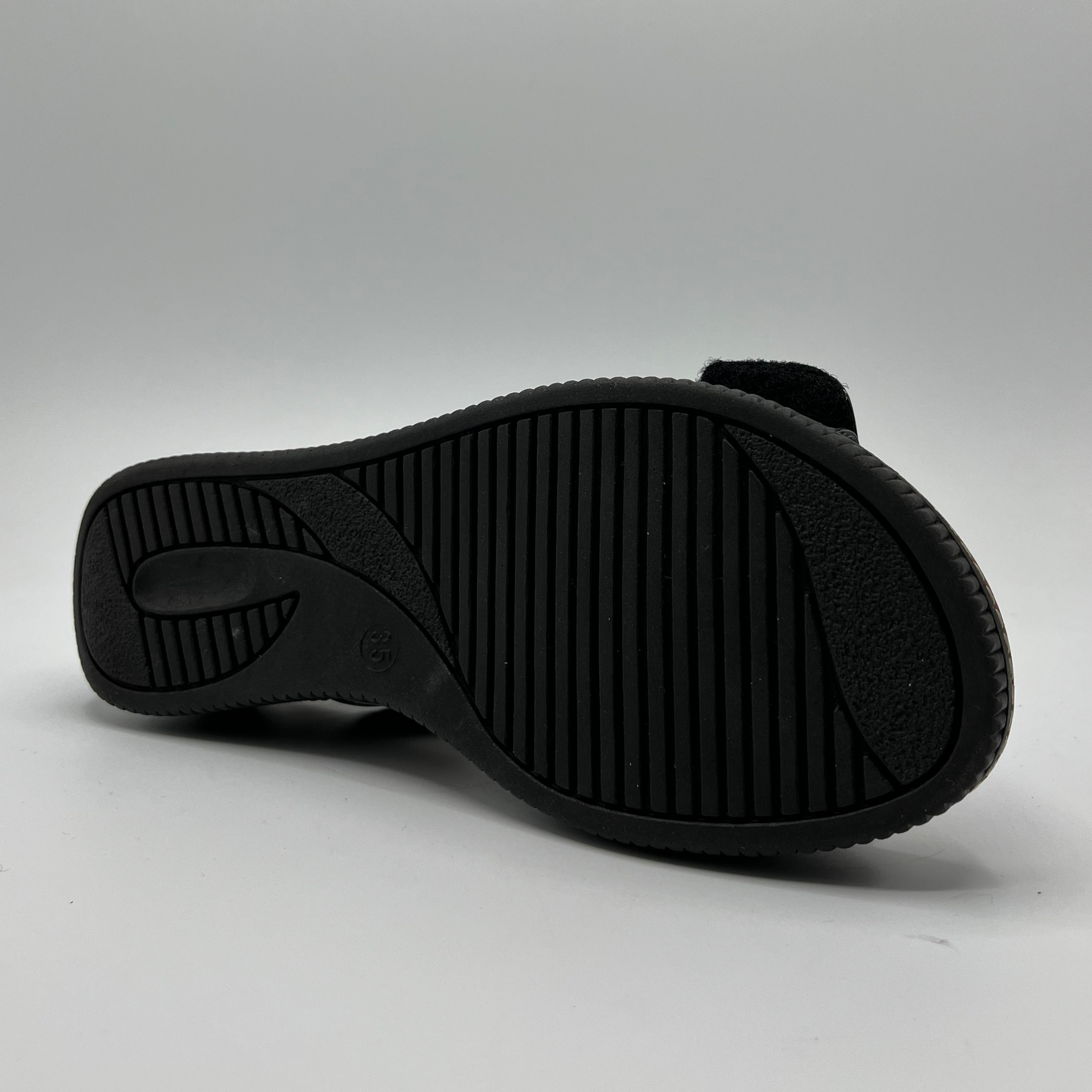 Bottom view of a black patent leather sandal with decorative gold buckles and a wedge heel.