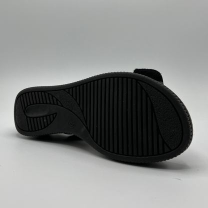 Bottom view of a black patent leather sandal with decorative gold buckles and a wedge heel.
