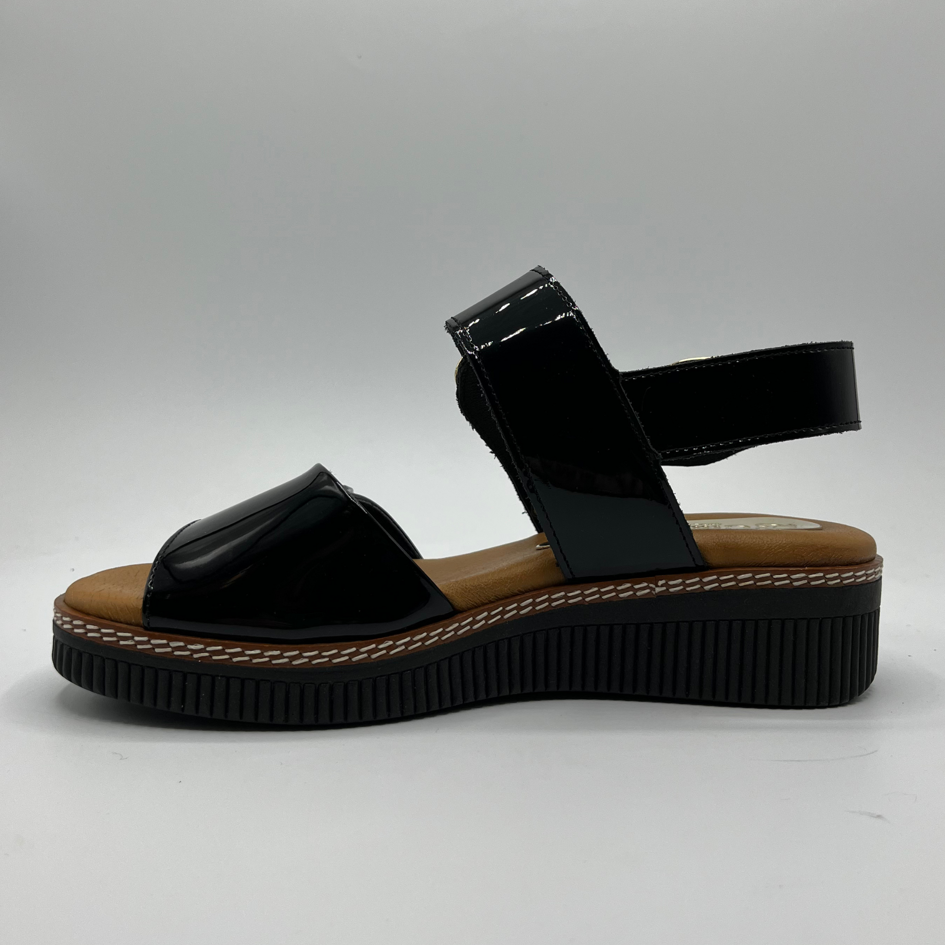 Left facing view of a black patent leather sandal with decorative gold buckles and a wedge heel.