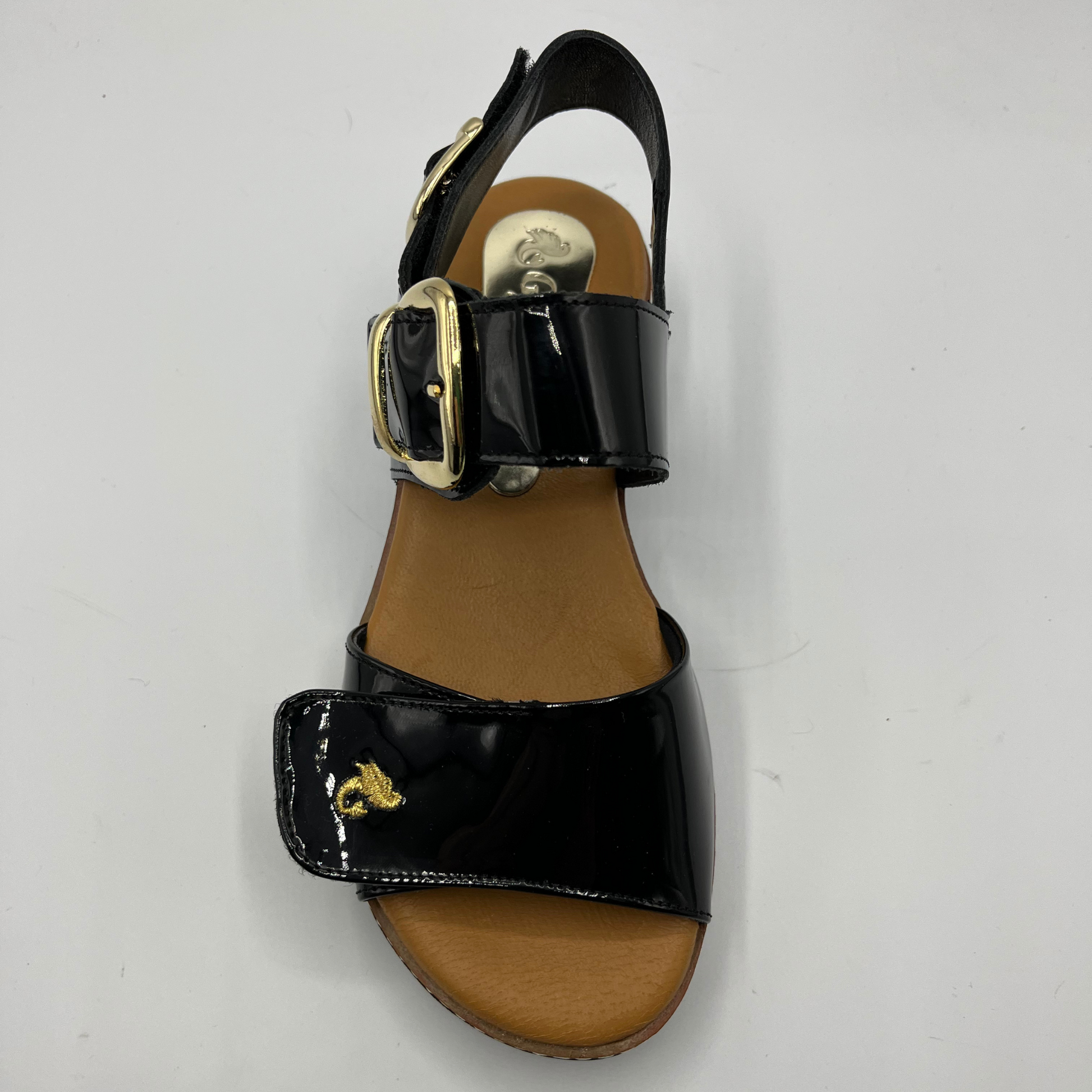 Top view of a black patent leather sandal with decorative gold buckles and a wedge heel.