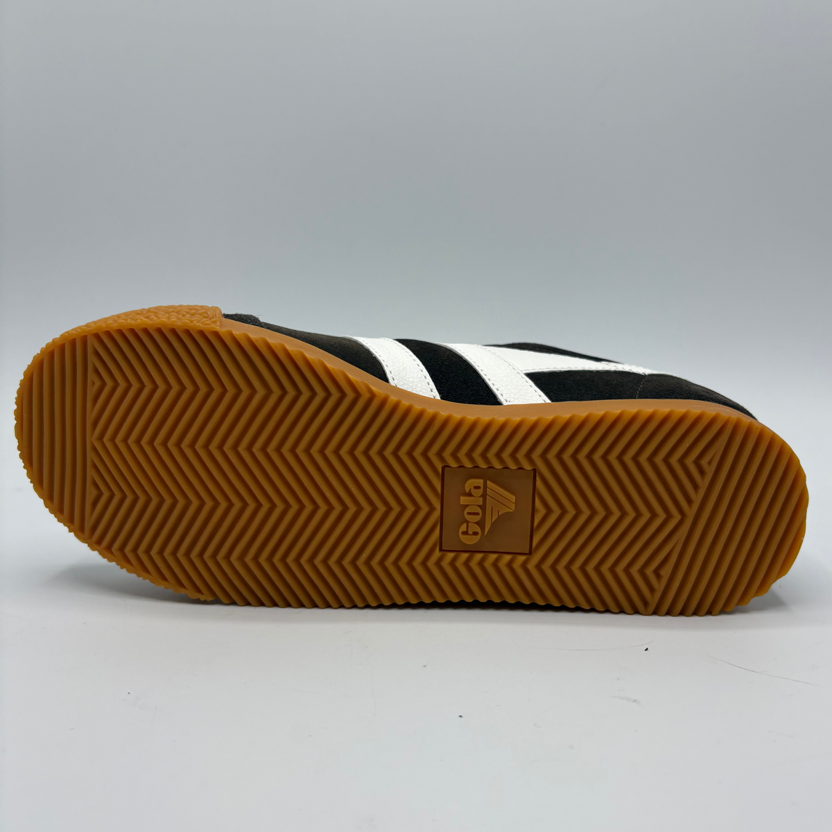 The outsole of a black and white shoe with a brown gum rubber sole, featuring the embossed Gola logo in the center.